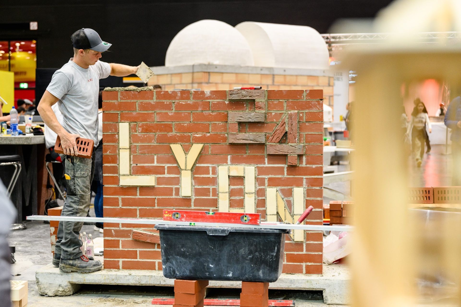 Maurer baut eine Ziegelmauer mit „LYON“ aus Leichtbausteinen. Auf der Mauer sitzen zwei Kuppeln.