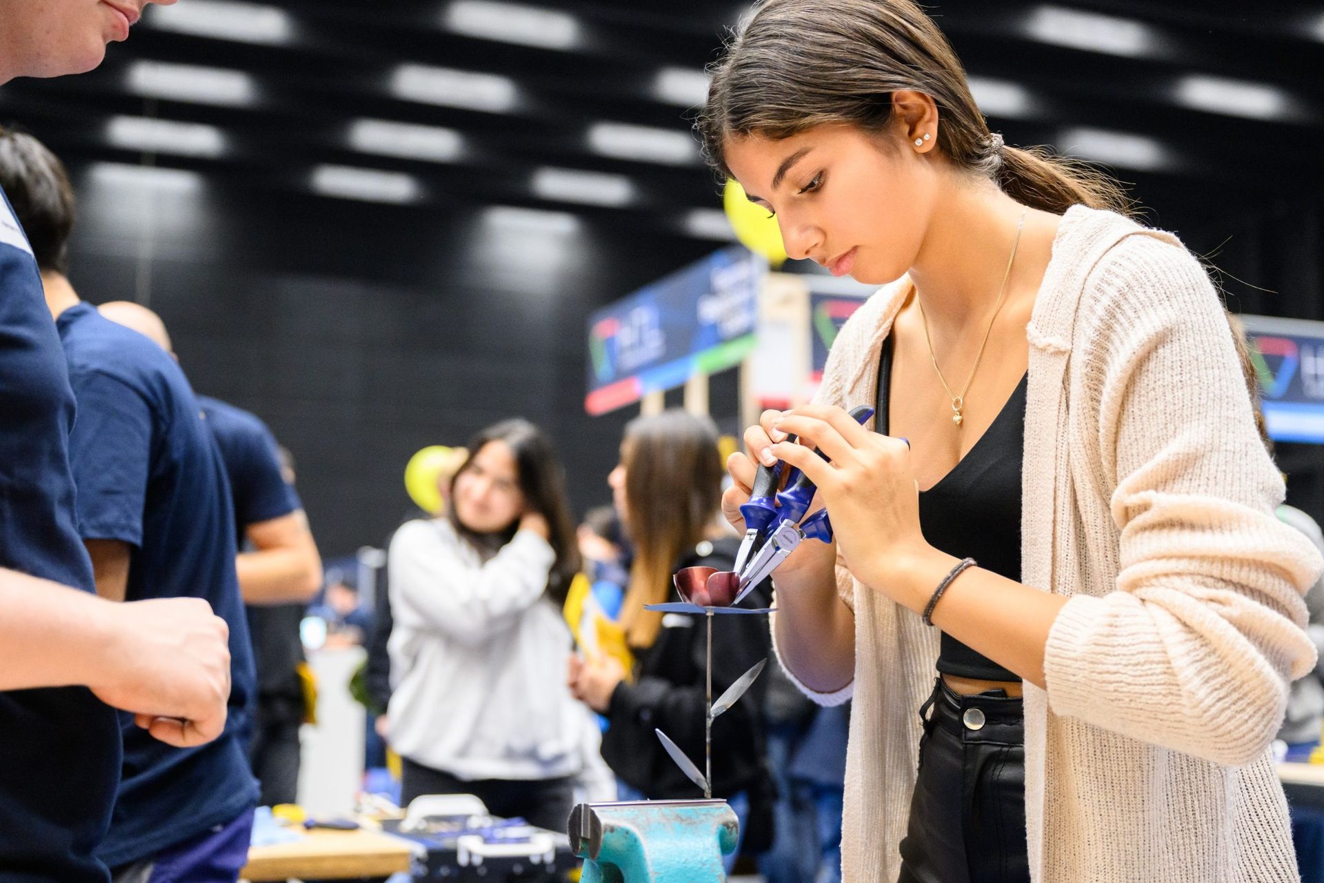 Eine junge Frau arbeitet bei einem Maker-Event konzentriert und mit Werkzeug an einem Projekt.