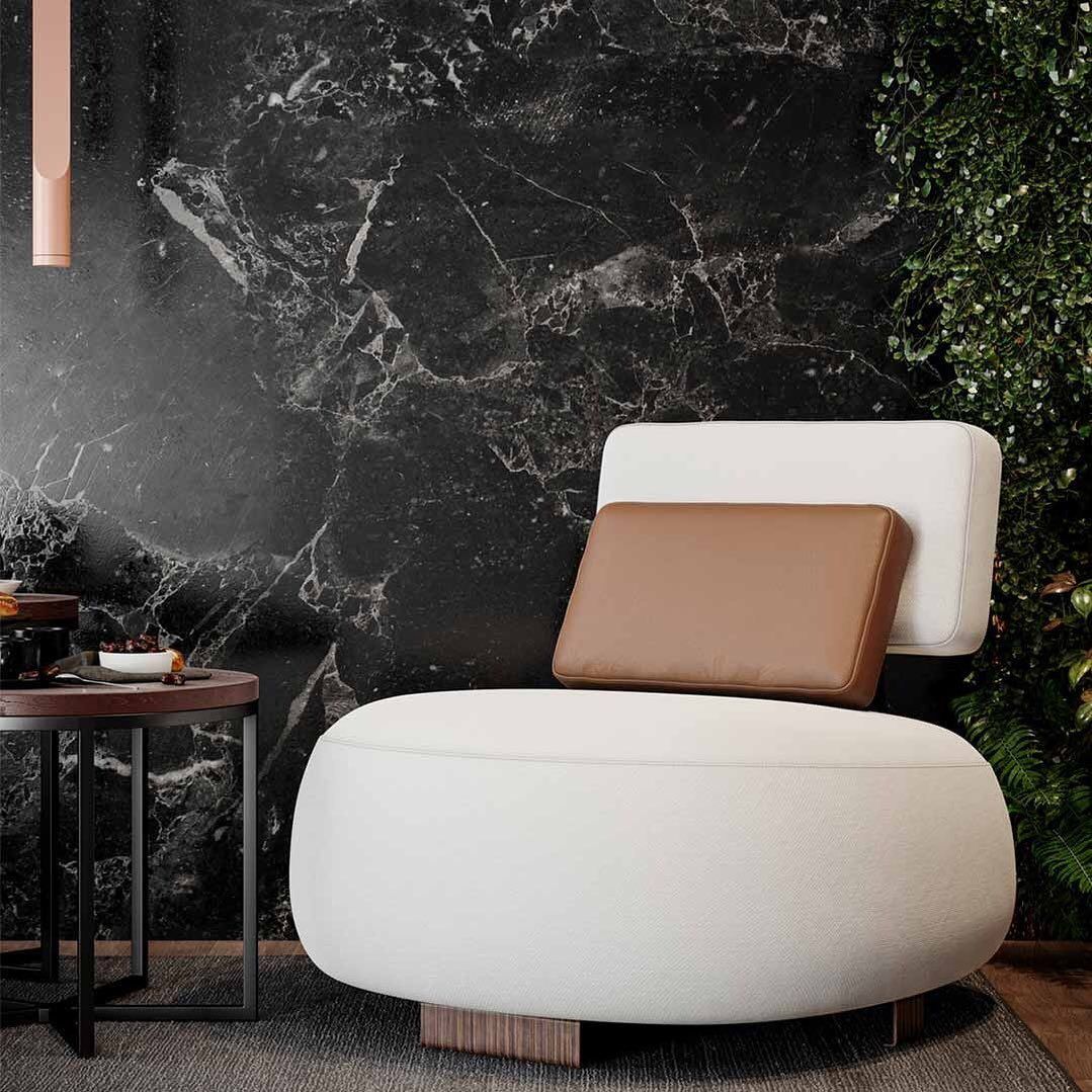 Uma cadeira branca com uma almofada marrom está em frente a uma parede de mármore preto.