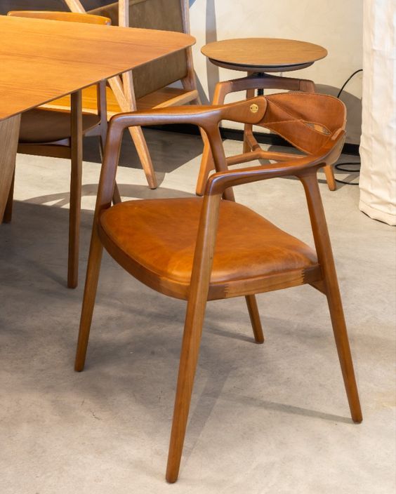 Uma cadeira de madeira com assento de couro marrom fica em frente a uma mesa