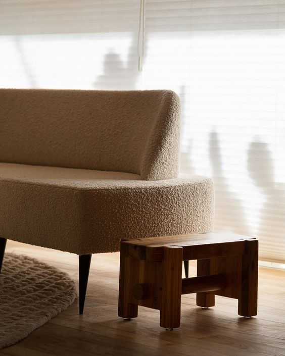 Um banquinho de madeira fica ao lado de um sofá na sala de estar.