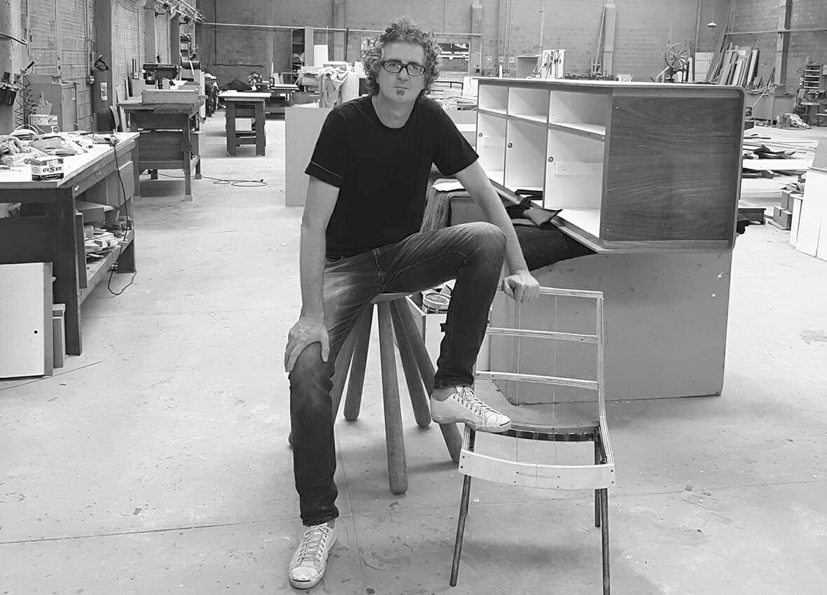 Um homem de camisa preta está sentado em uma cadeira em uma sala.