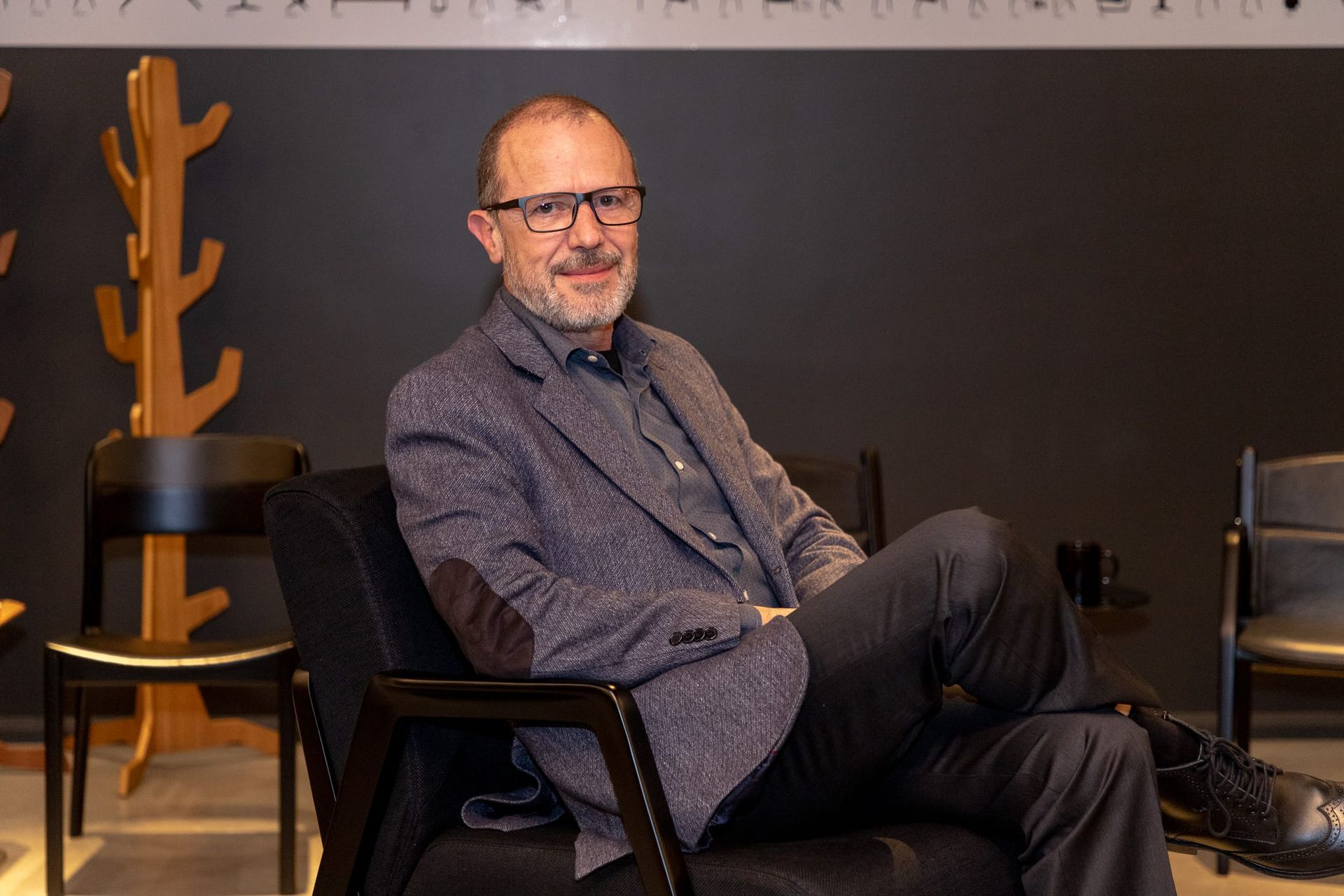 Um homem de terno e óculos está sentado em uma cadeira.