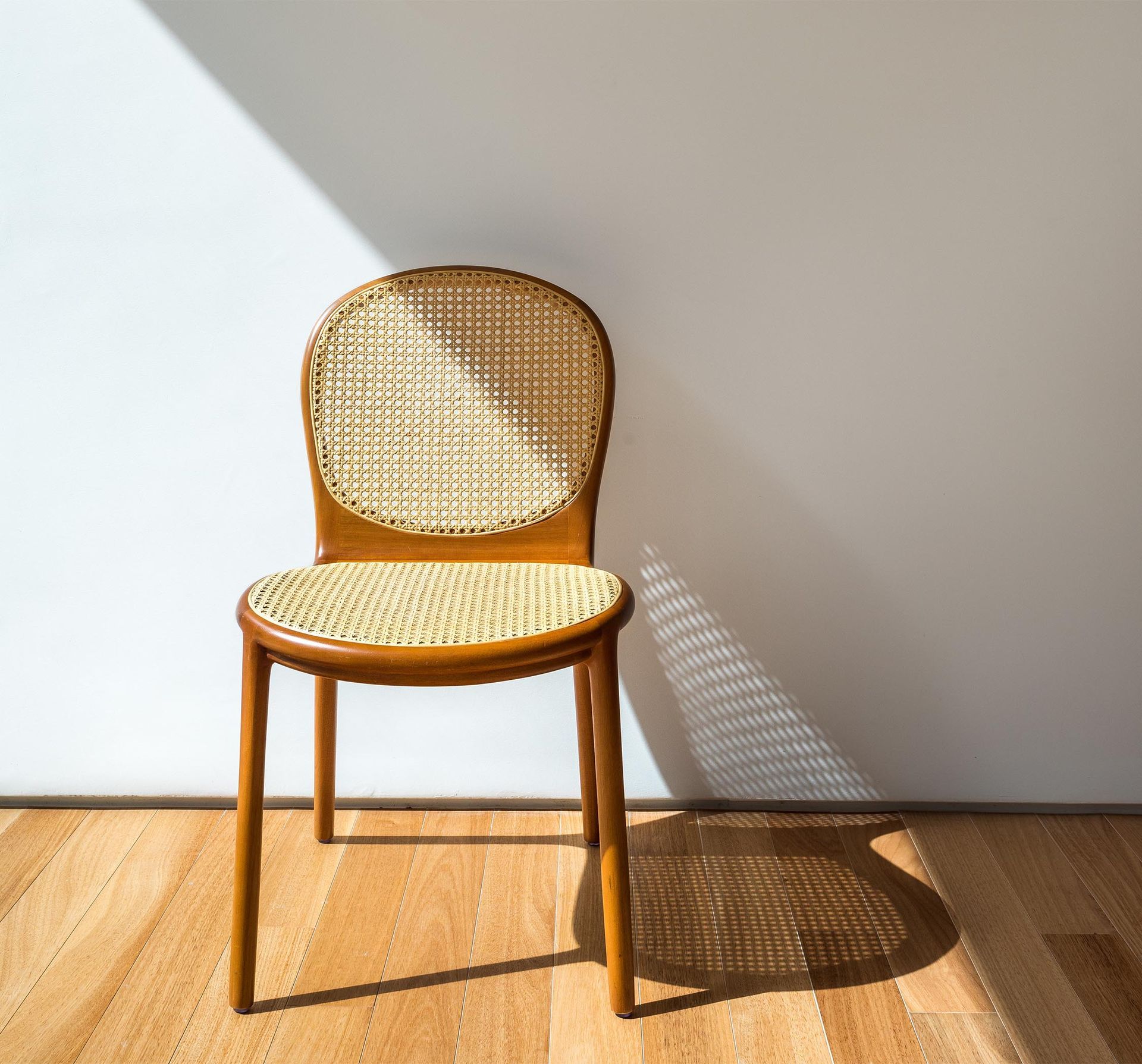Uma cadeira de vime está apoiada em um piso de madeira em frente a uma parede branca.