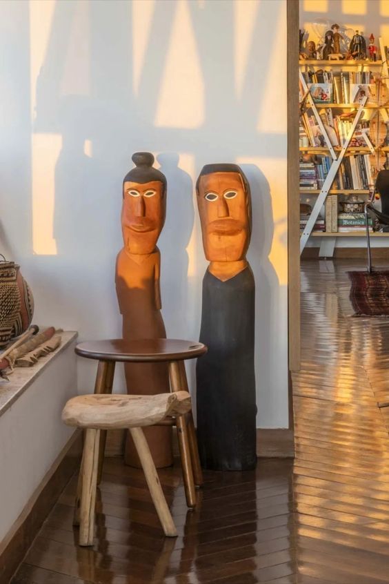 Duas esculturas estão sentadas em um banquinho de madeira em uma sala