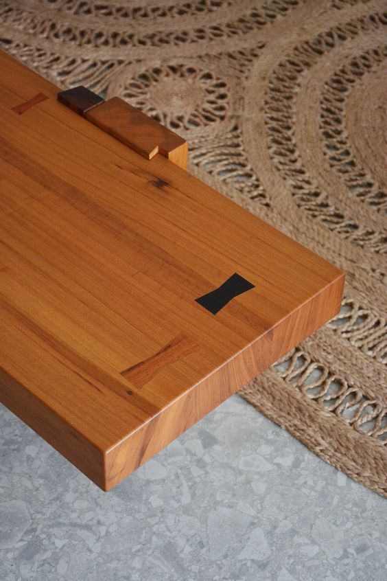 Uma mesa de madeira está sobre um piso de concreto ao lado de um tapete.