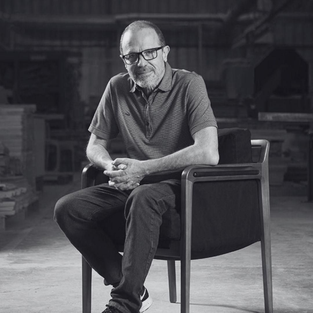 Um homem de óculos está sentado em uma cadeira em uma foto em preto e branco.