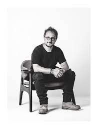 Um homem está sentado em uma cadeira com as mãos cruzadas.