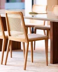 Uma cadeira de madeira com encosto de vime está ao lado de uma mesa de jantar.