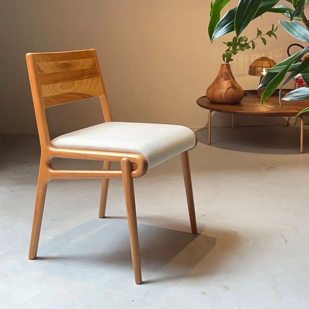 Uma cadeira de madeira com assento branco fica ao lado de uma mesa