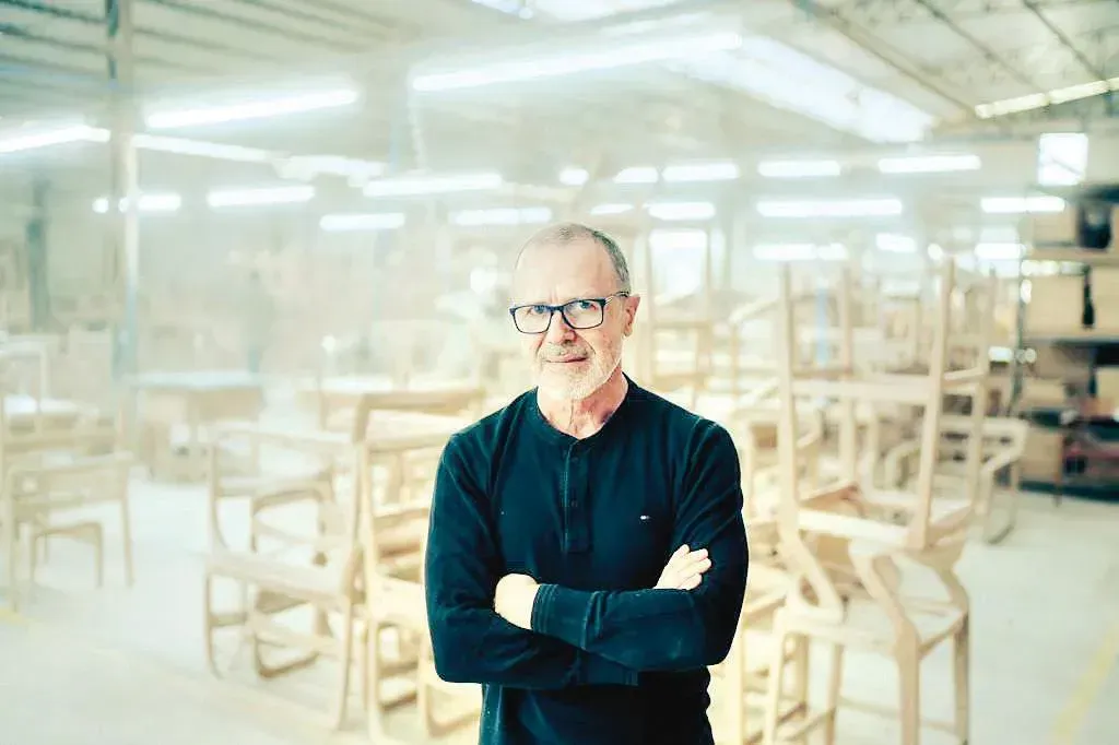 Um homem está em uma fábrica com os braços cruzados.