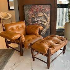 Uma cadeira e pufe de couro marrom em uma sala de estar com uma pintura na parede.