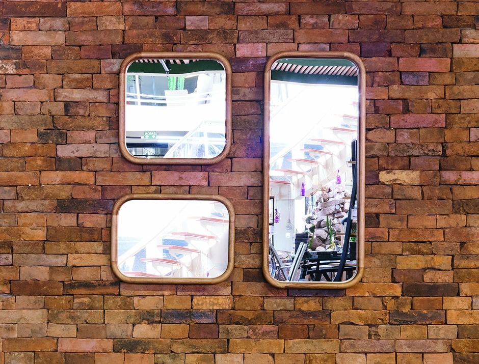 Três espelhos estão pendurados em uma parede de tijolos.