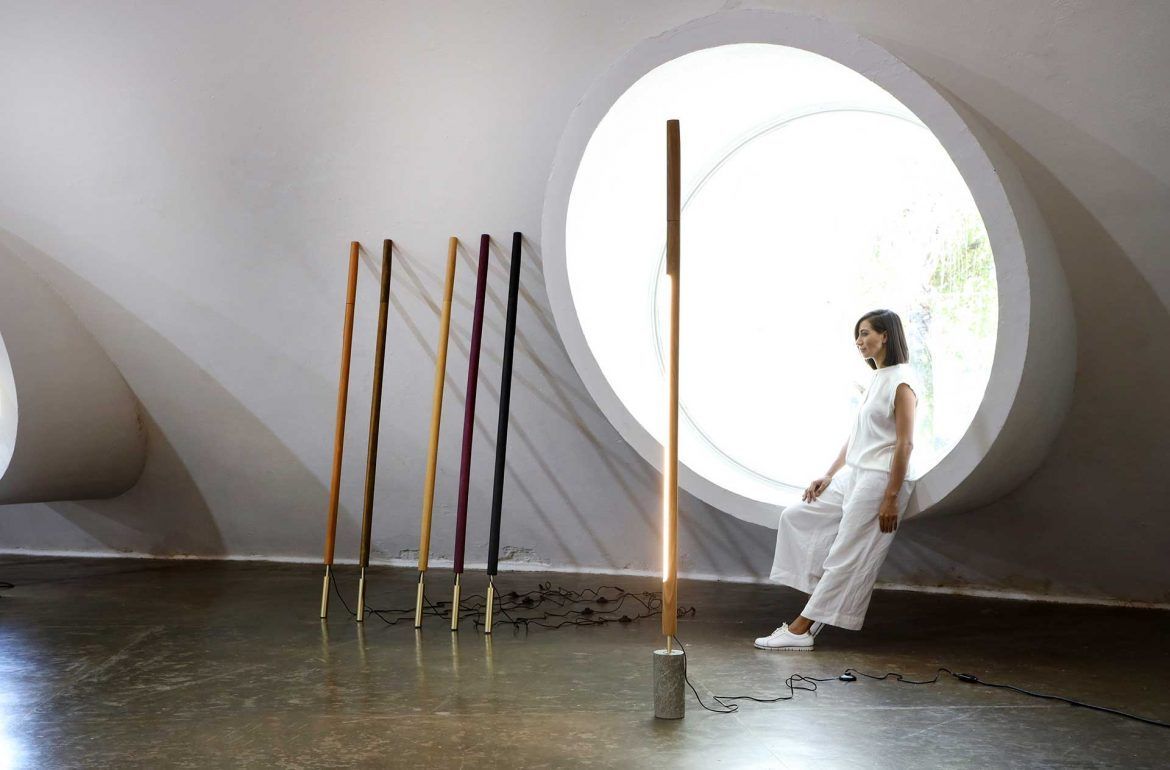 Uma mulher de vestido branco está parada em frente a uma janela redonda.
