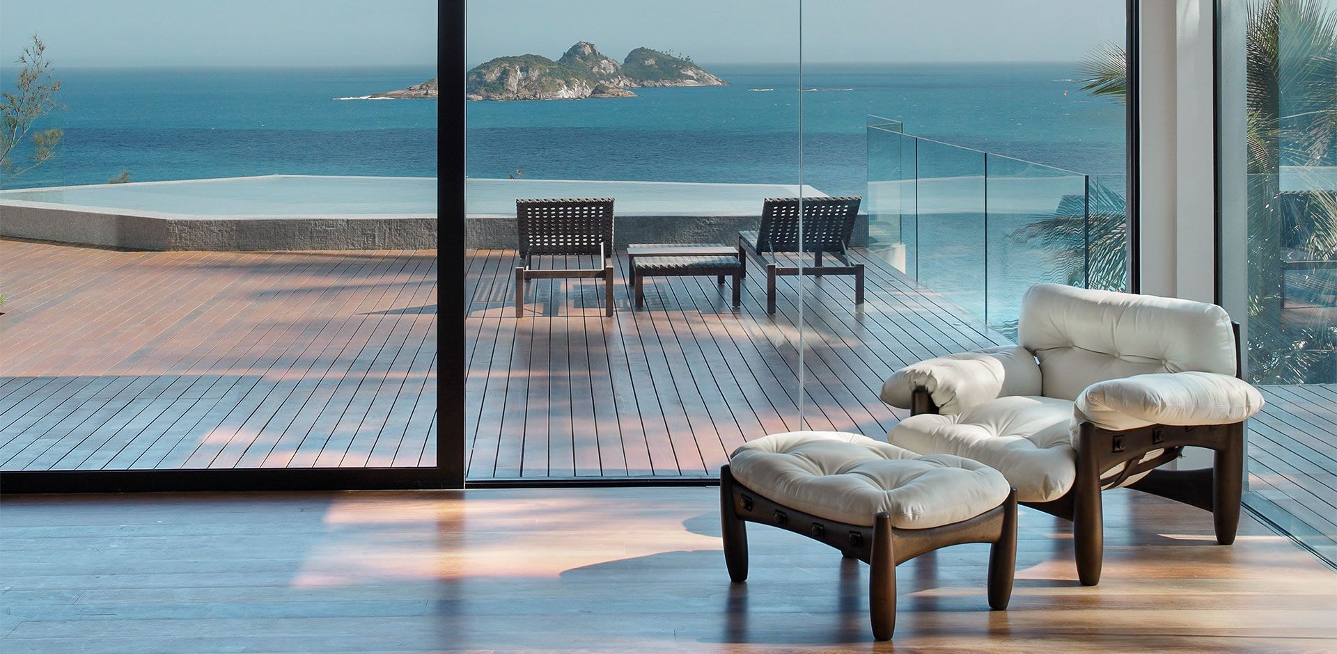 Uma sala de estar com cadeira e pufe e vista para o mar