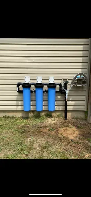 Three blue water filters are hanging on the side of a house.