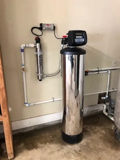 A stainless steel water filter is sitting on the floor next to a wall.