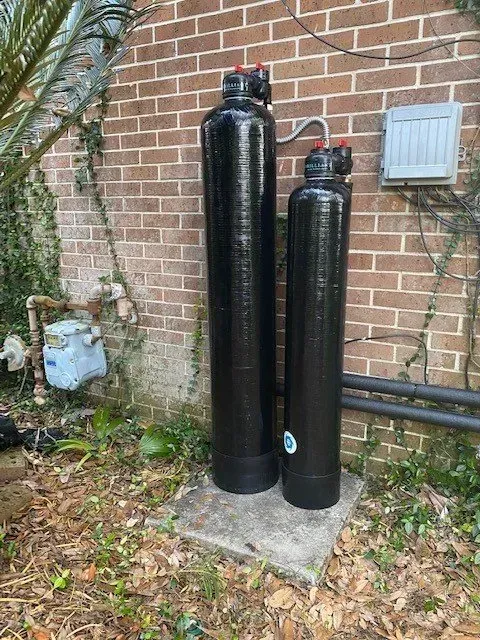 Two black water filters are sitting next to each other in front of a brick wall.