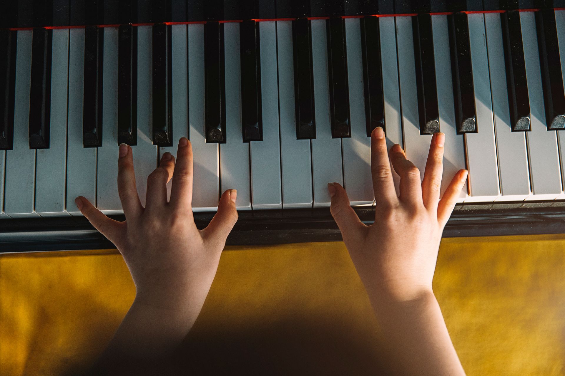 Mani che suonano un pianoforte. Tasti bianchi e neri, mani di bambino, luce del sole.