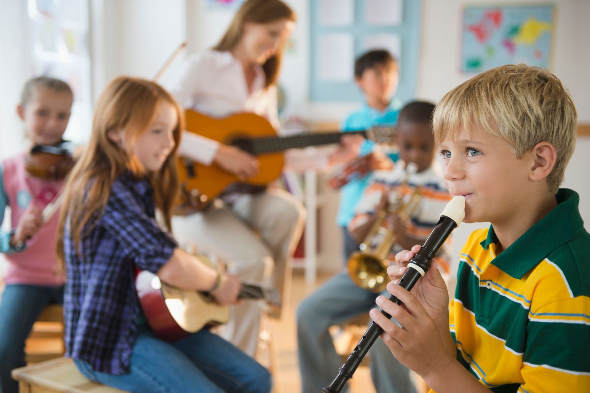 Bambini che suonano uno strumento in classe; un insegnante suona la chitarra.