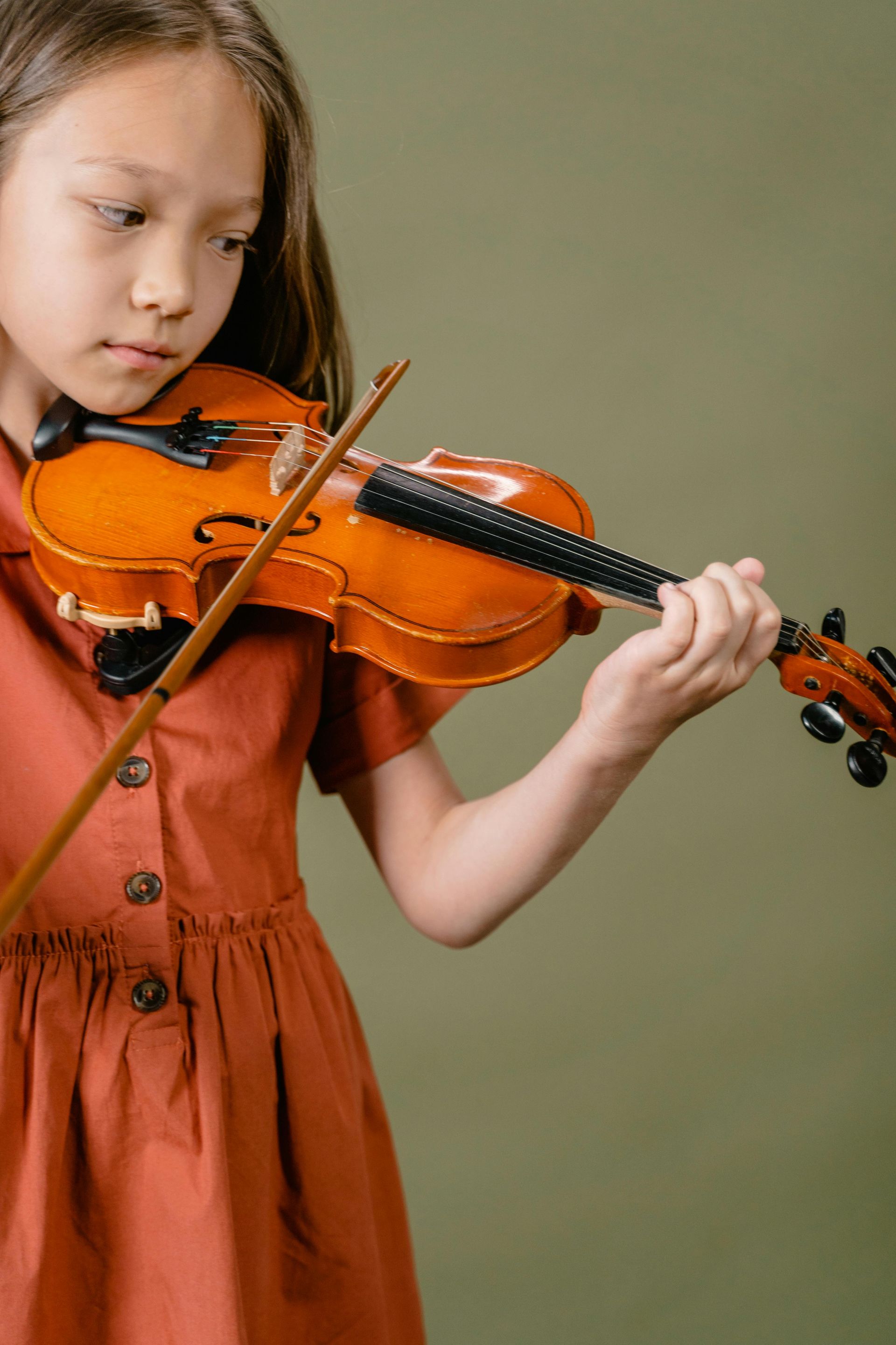 Ragazza che suona il violino, indossa un abito color ruggine, su uno sfondo verde tenue.