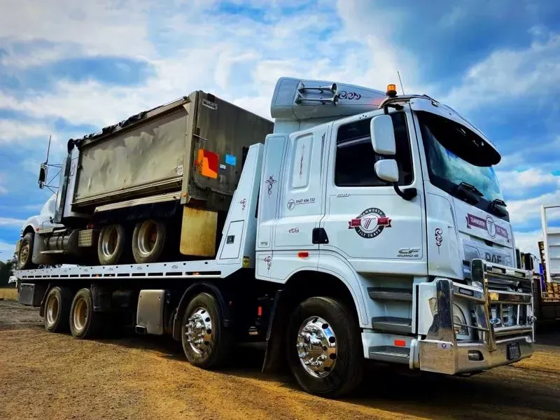 A White Flatbed Tow Truck Transporting a Dark, Industrial Dump Truck — Tamworth Tilt Trays in Tamworth, NSW