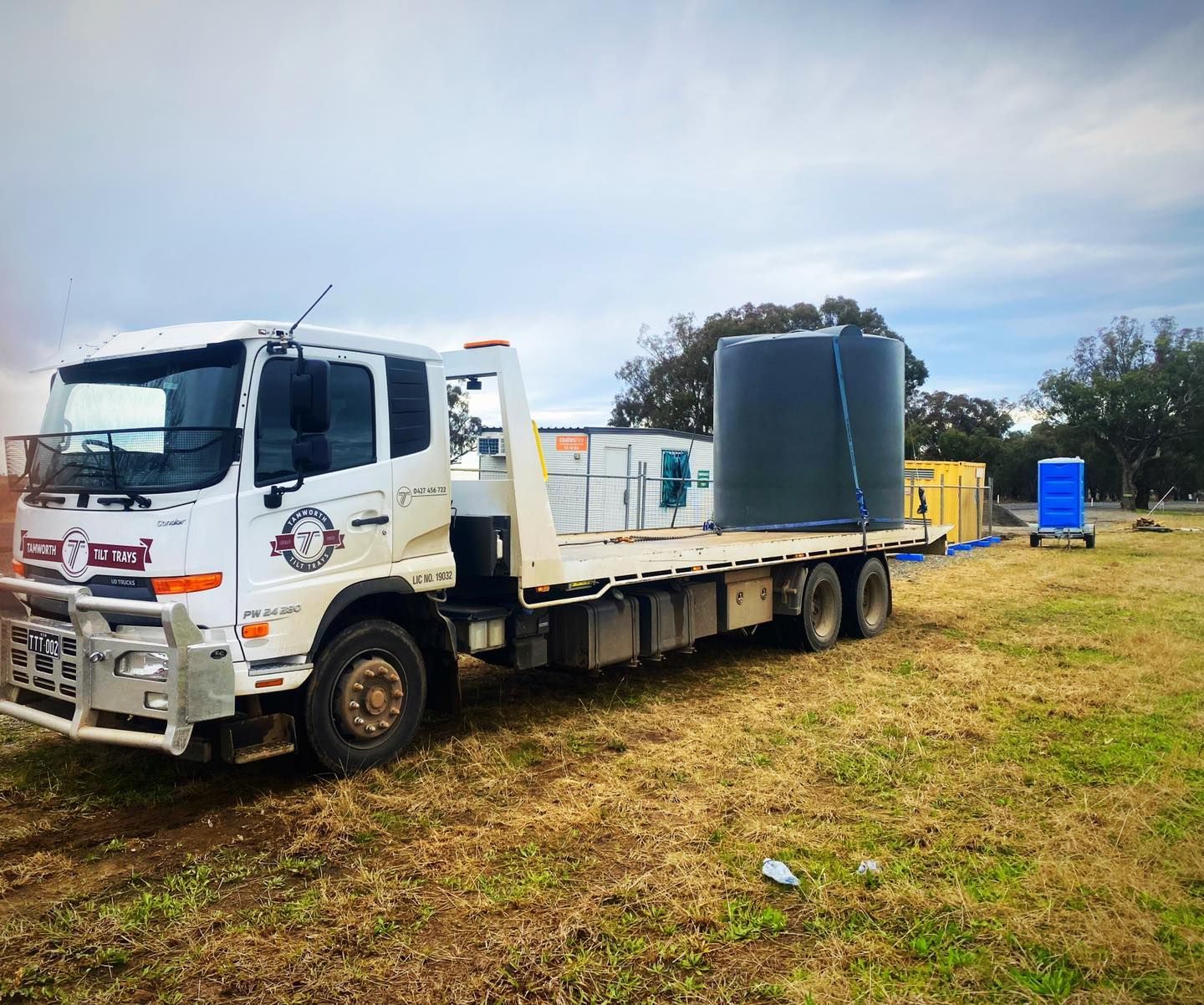 White Flatbed Truck Carrying Large Blue Tank On A Grassy Field — Tamworth Tilt Trays in Tamworth, NSW