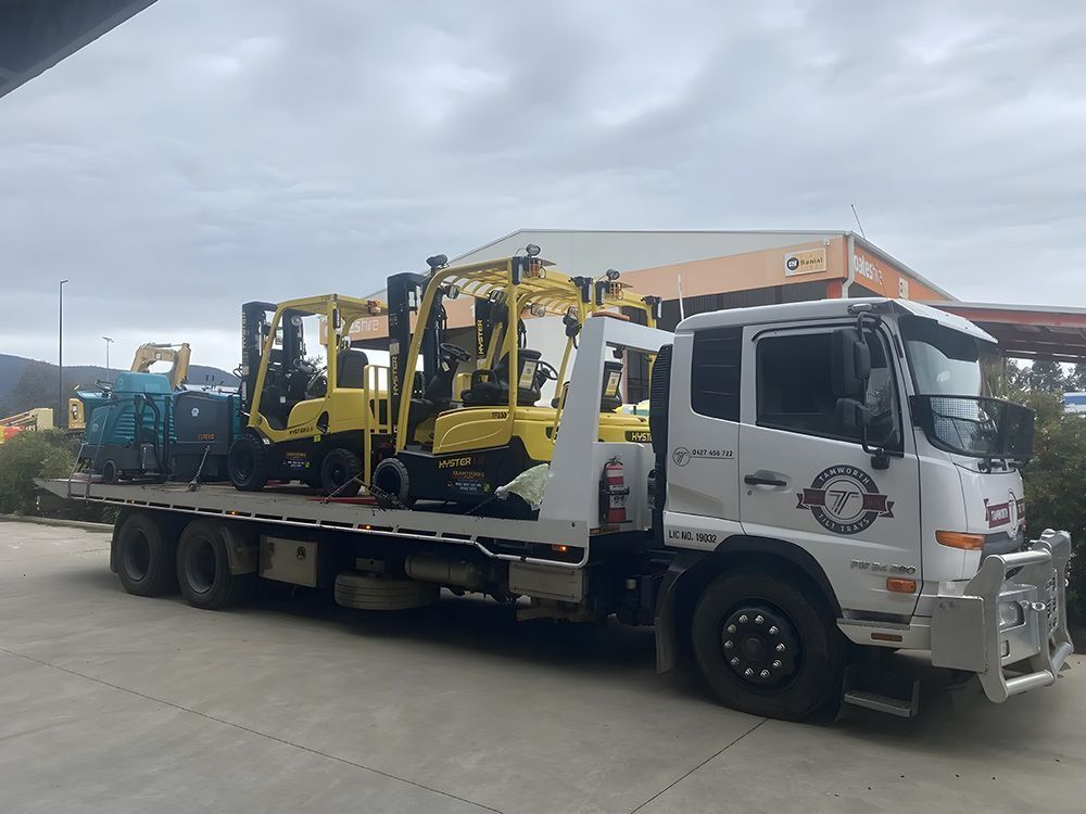 A White Flatbed Truck Carrying Several Yellow Construction Vehicles — Tamworth Tilt Trays in Tamworth, NSW