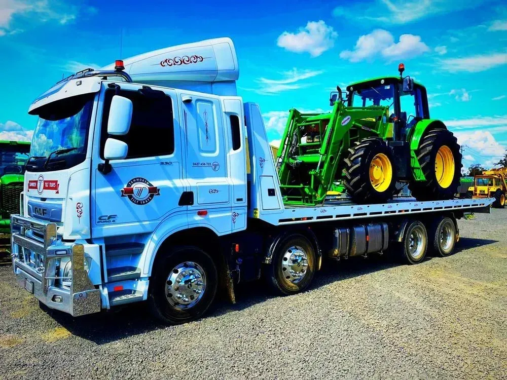 A White Flatbed Tow Truck Transporting a Green Tractor — Tamworth Tilt Trays in Tamworth, NSW