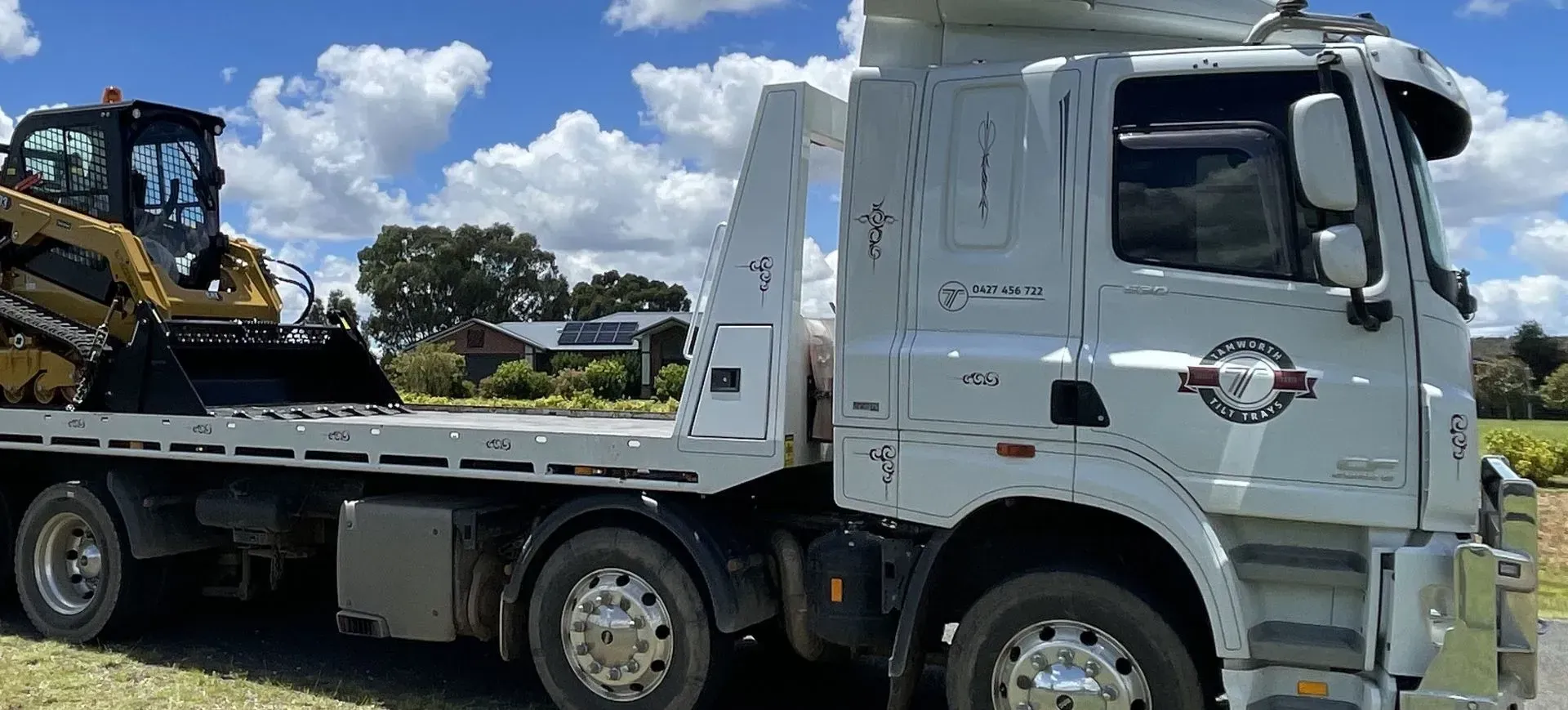 A White Flatbed Truck Parked Outdoors, Carrying a Yellow Skid-Steer Loader — Tamworth Tilt Trays in Tamworth, NSW