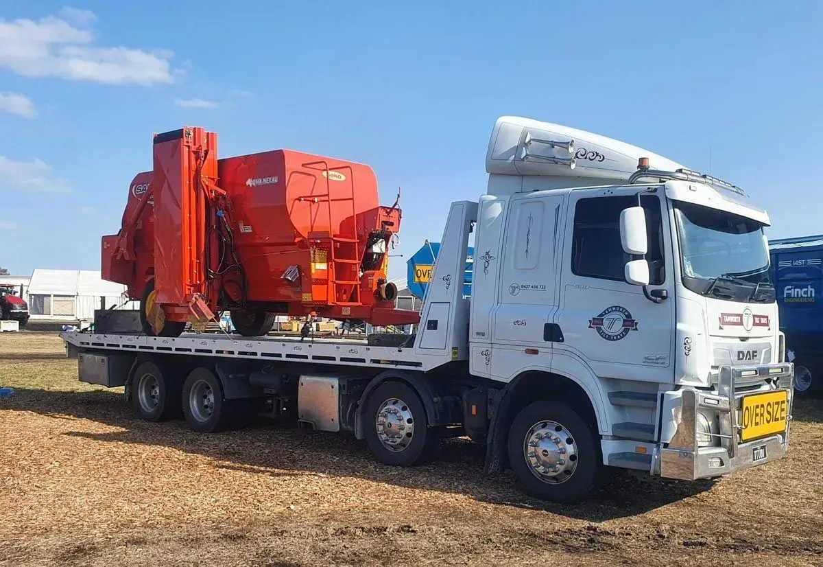 A White Flatbed Truck Transporting a Large, Bright Orange Agricultural Mixing Machine — Tamworth Tilt Trays in Tamworth, NSW