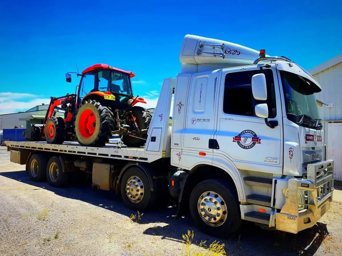 A White Flatbed Truck Parked Outdoors, Carrying a Bright Orange Tractor on Its Bed — Tamworth Tilt Trays in Tamworth, NSW
