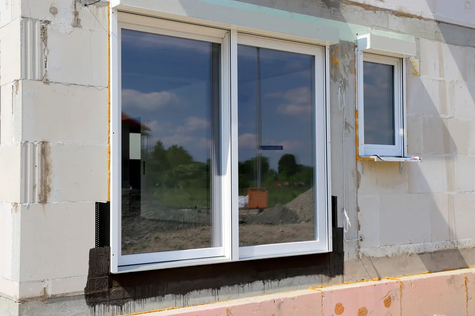 White framed windows on a partially constructed building with reflective glass, showing exterior view.