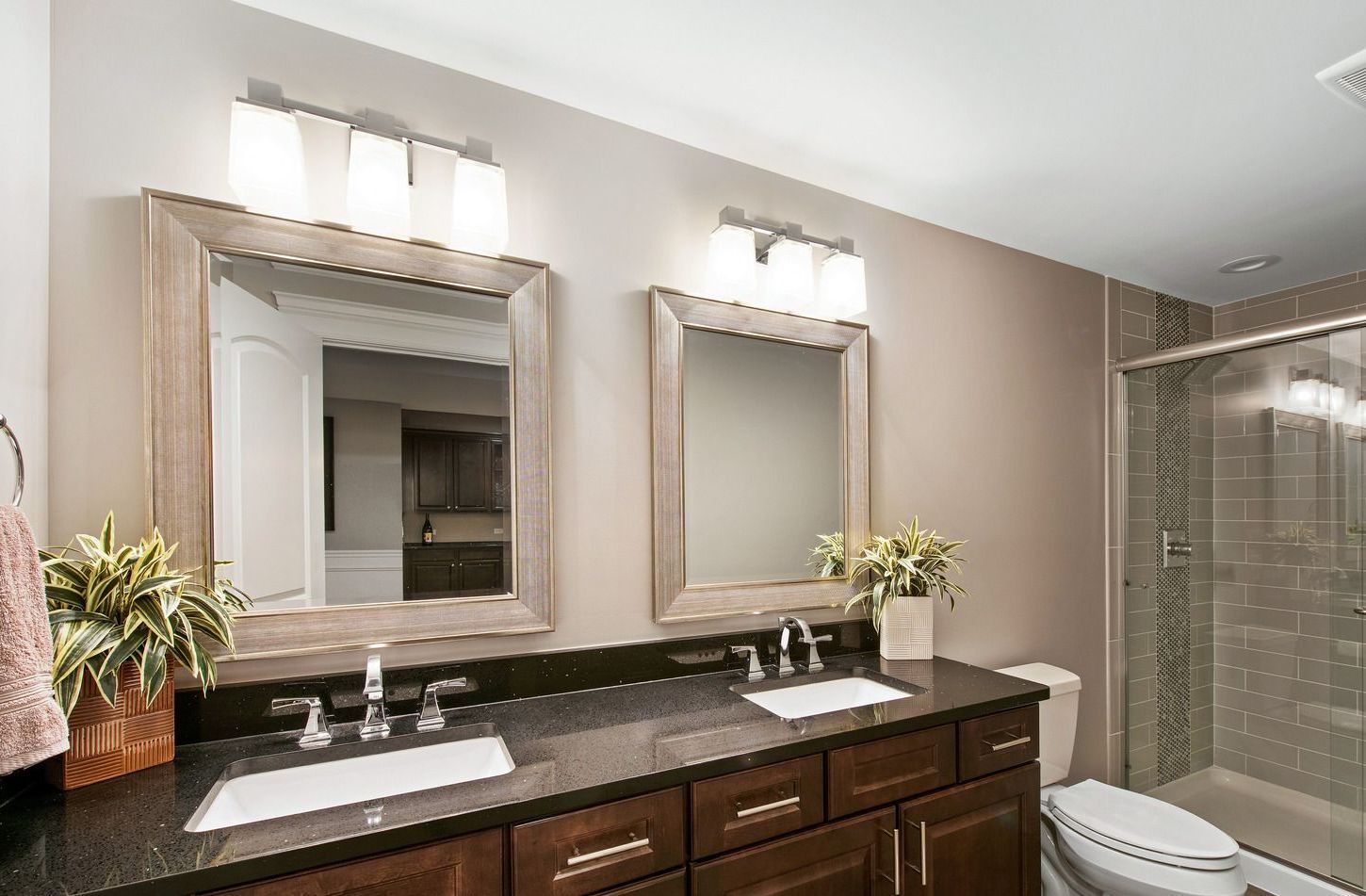 Bathroom with two sinks, mirrors, and a shower; dark cabinets, black countertop, and neutral wall color.