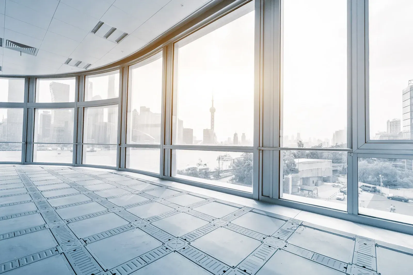 Bright, empty office space with large windows showcasing a city skyline on a sunny day.