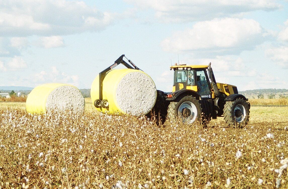 A tractor fitted with a McCormack Wheelie Grab is transporting a round cotton bale.