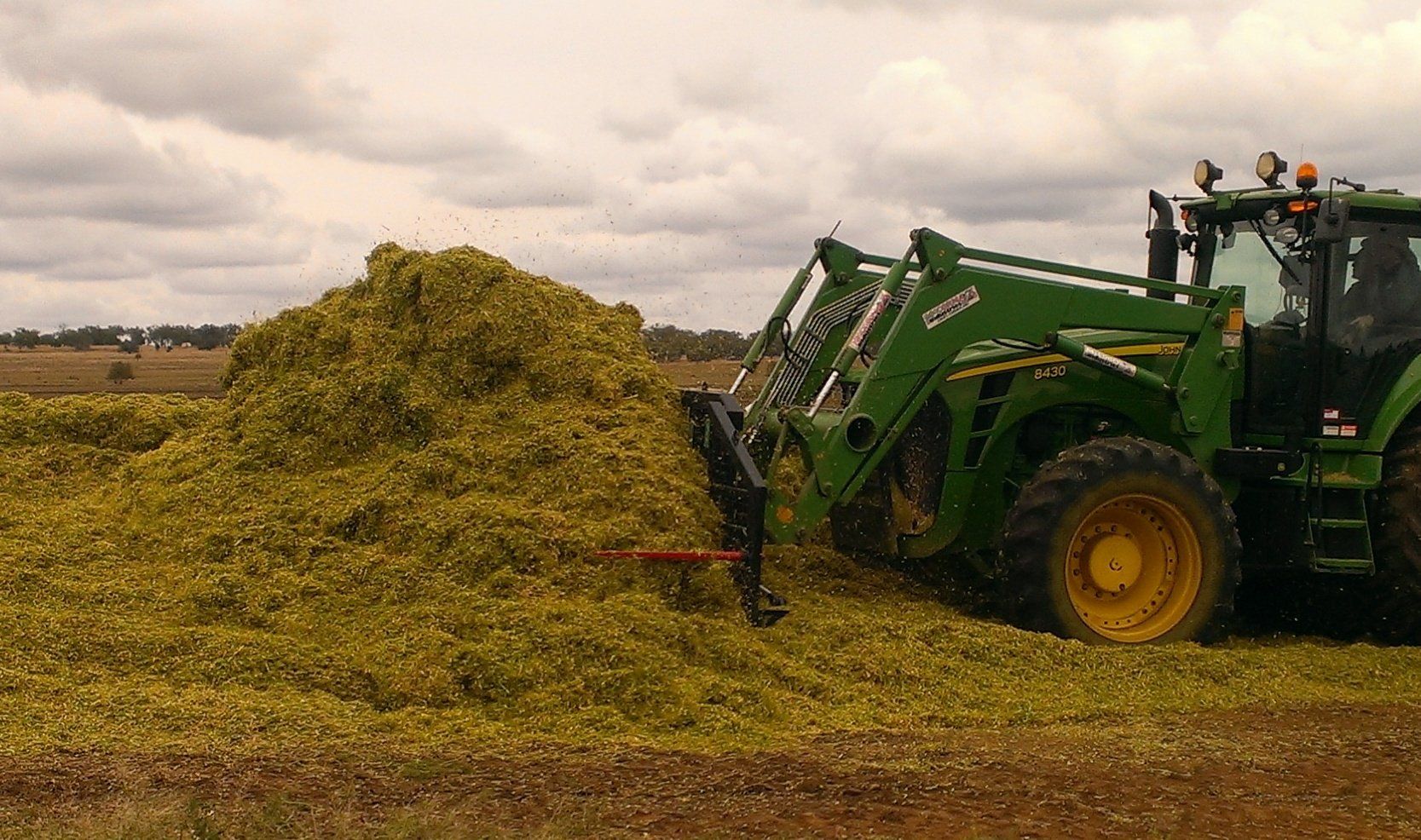 a photo of a McCormack Silage Buck Rake Attachment in use, fitted to a John Deere tractor