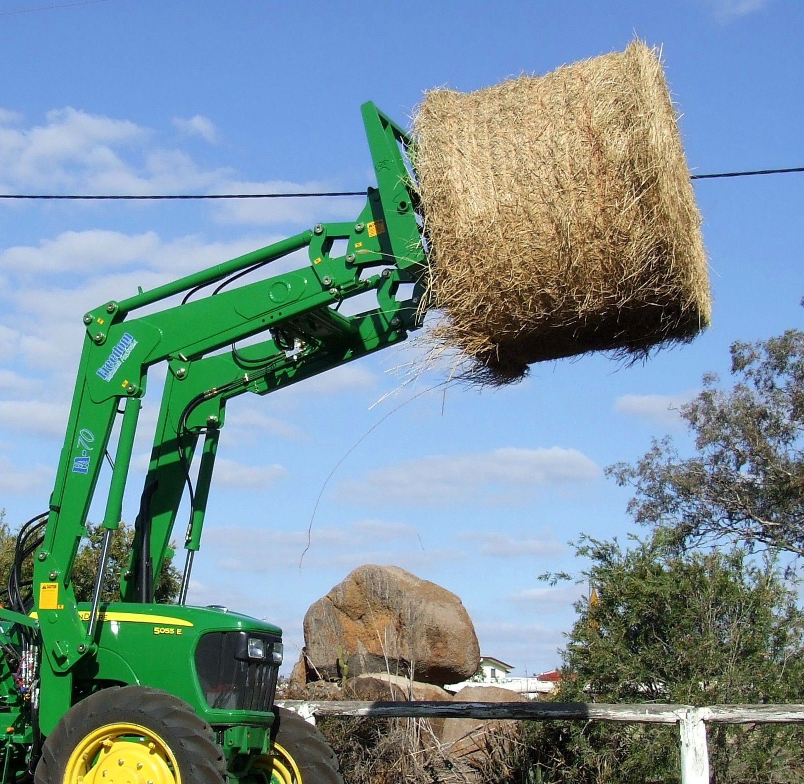 A green john deere tractor is lifting a bale of hay