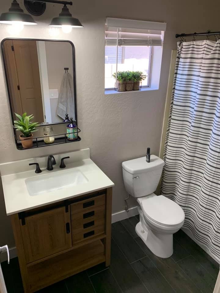 A bathroom with a toilet , sink , mirror and shower curtain.