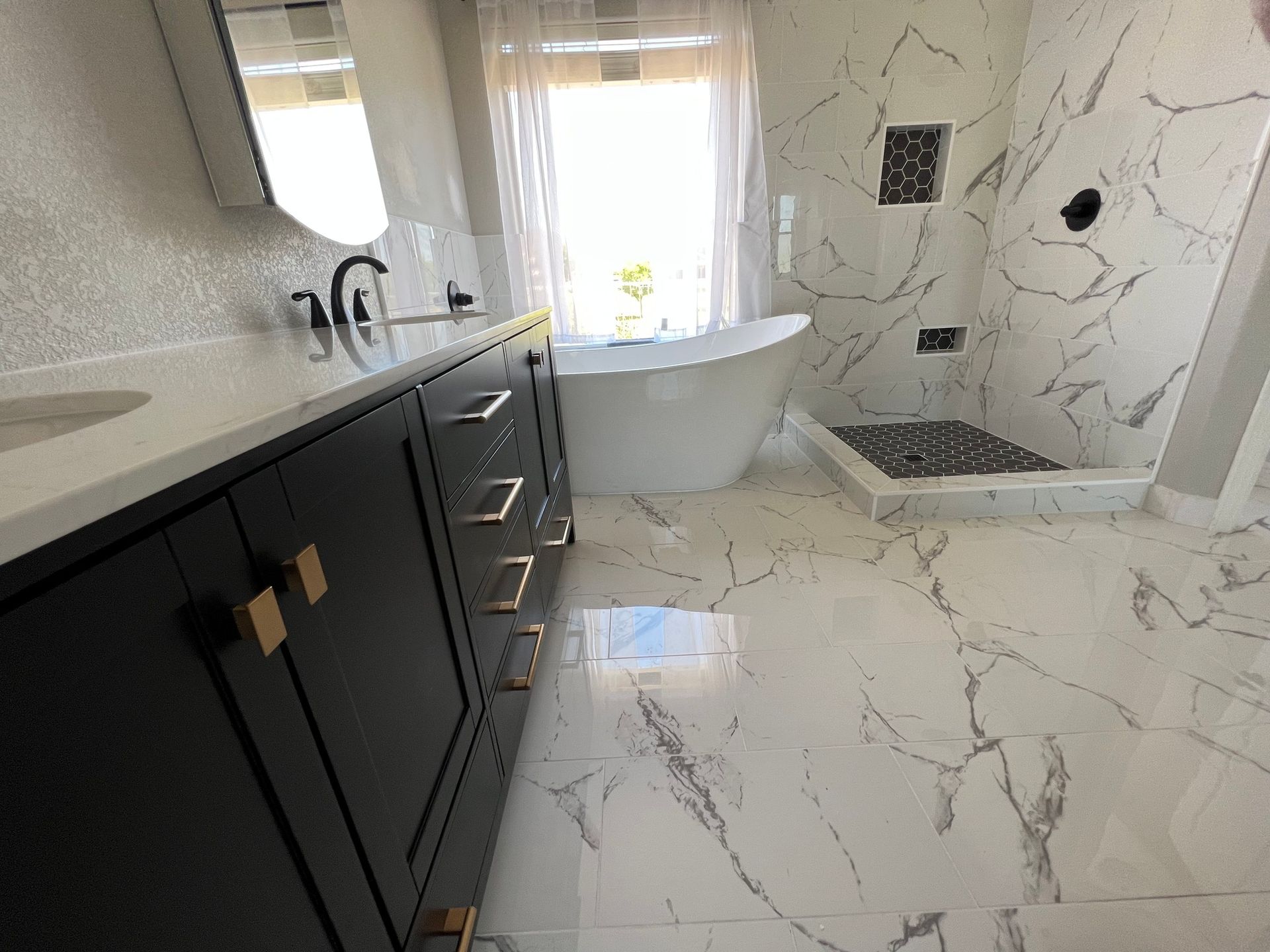 Modern bathroom with black vanity, freestanding tub, walk-in shower, and marble-patterned tile floor and walls