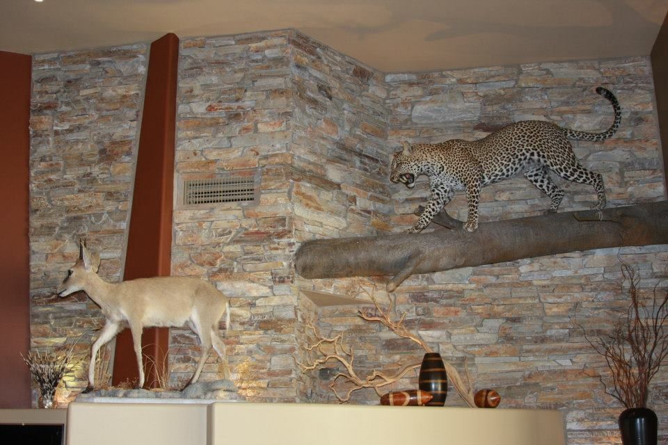 A leopard is standing on a tree branch next to a deer statue.