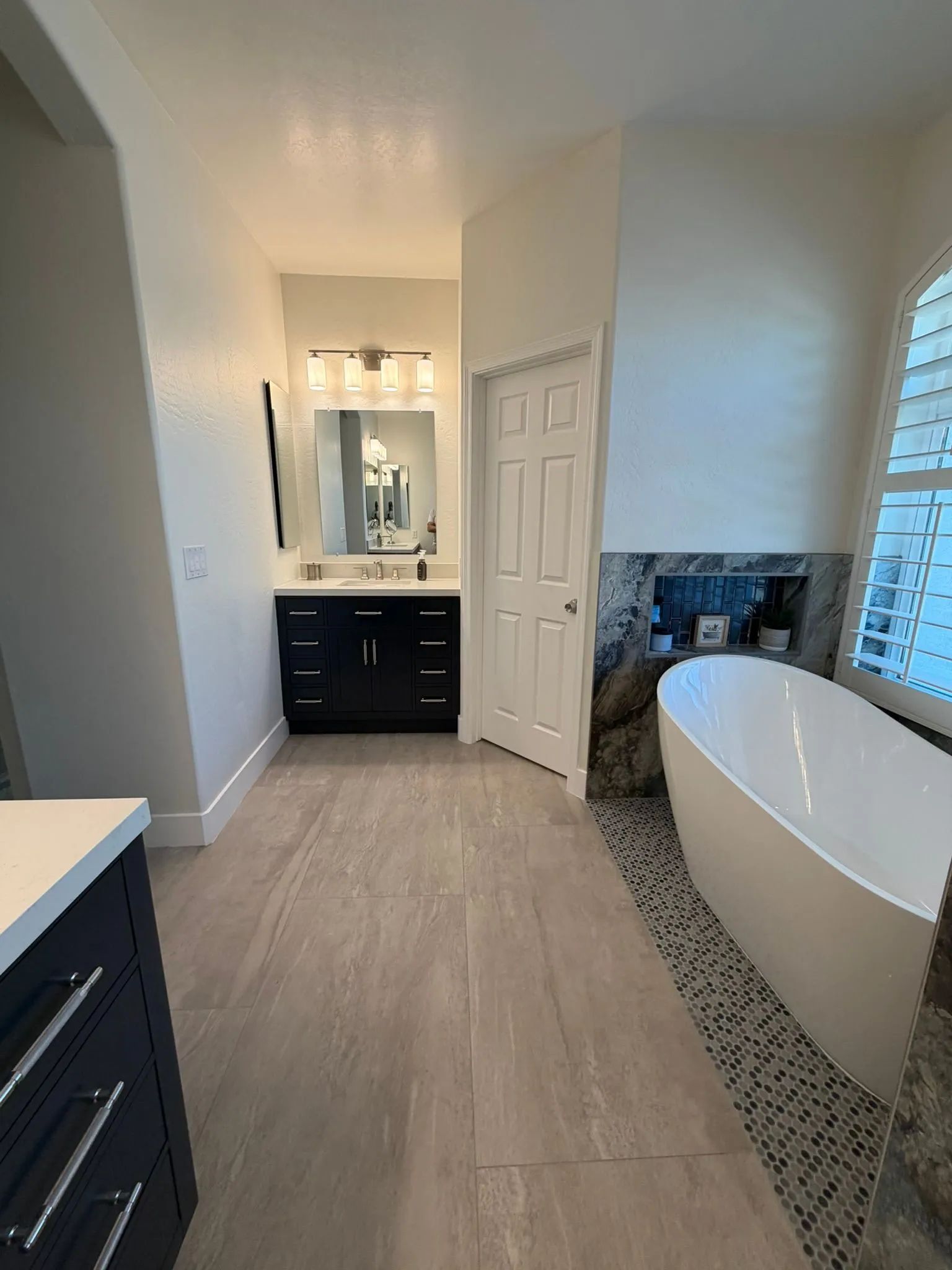 Modern bathroom with double vanity, walk-in shower, and freestanding tub on pebble tile floor