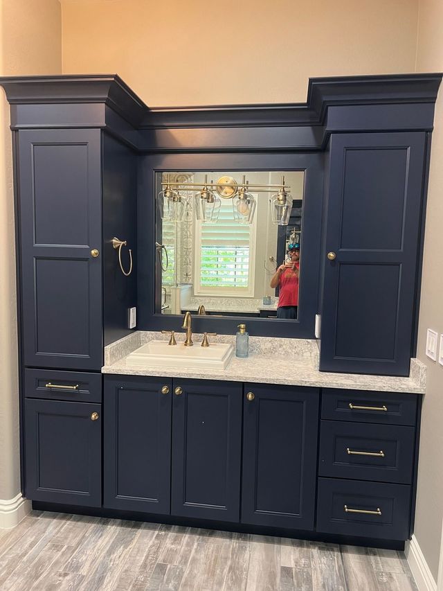Navy bathroom vanity with marble countertop, large mirror, and cabinet storage against beige walls.