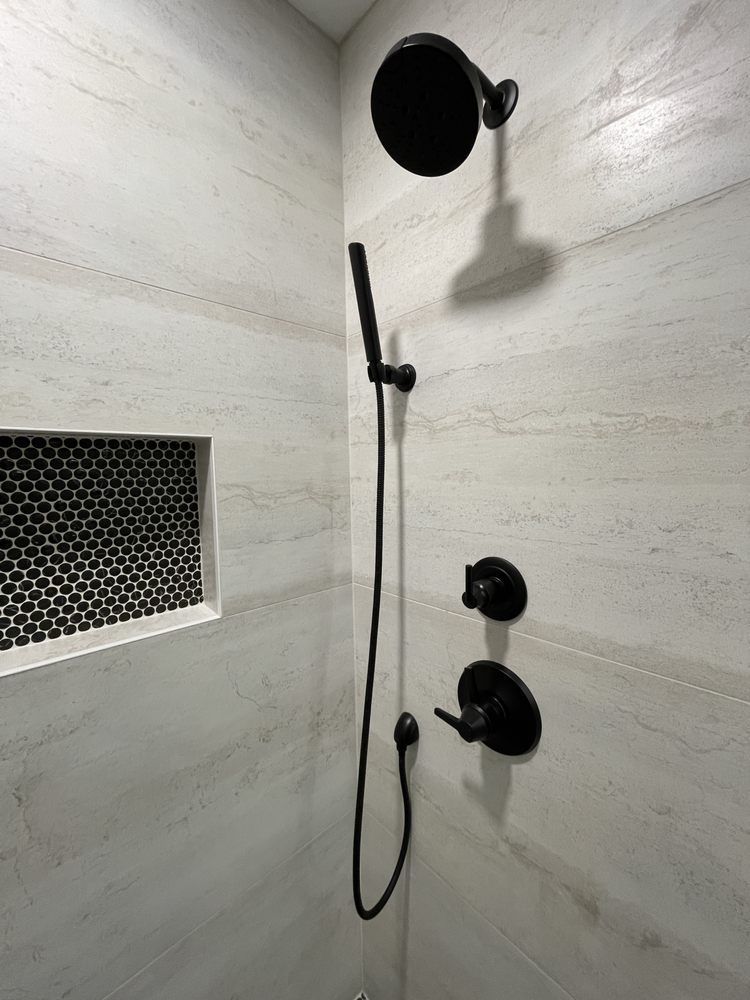 A shower with a black shower head and black faucets.