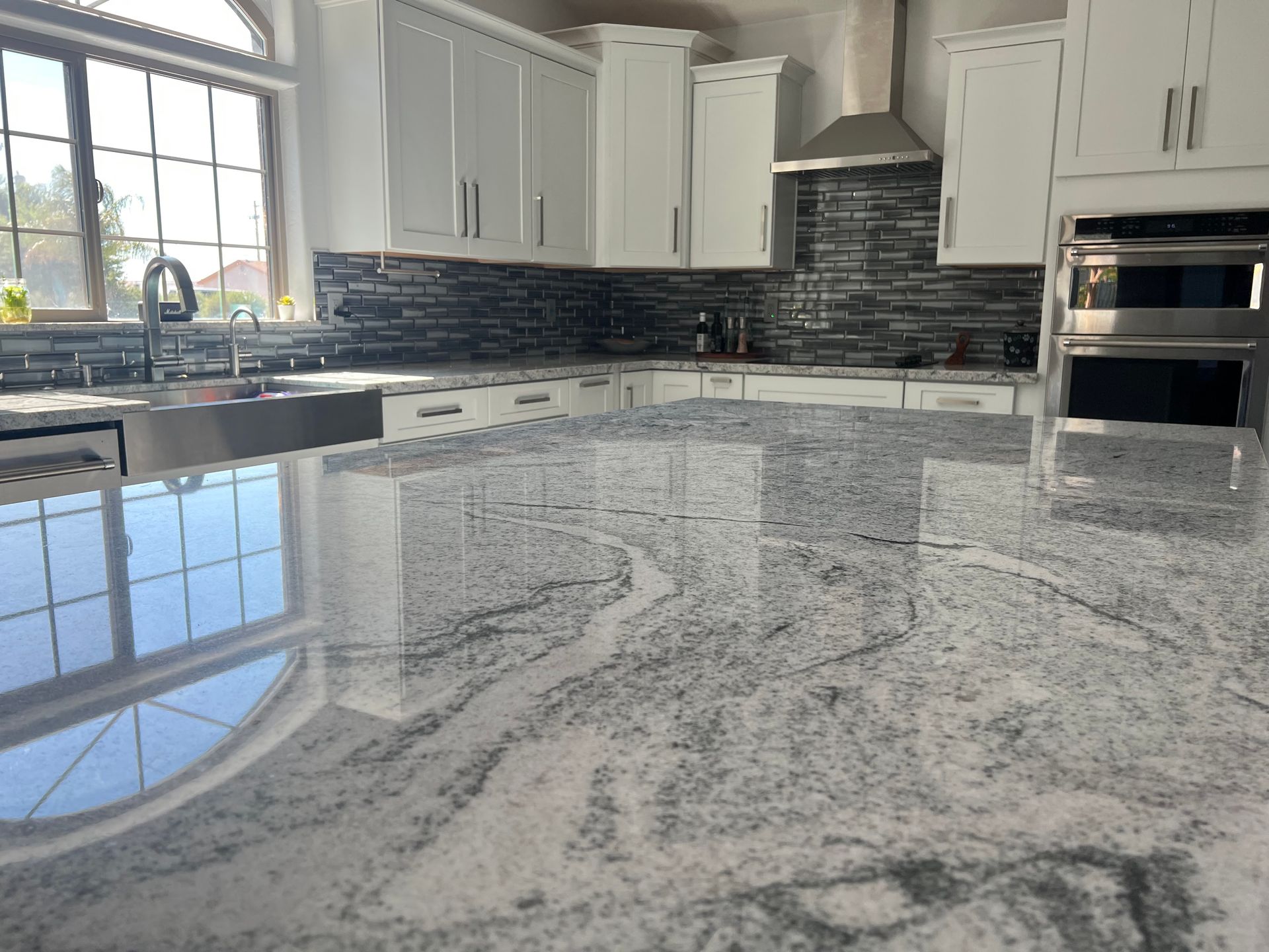 A kitchen with granite counter tops , white cabinets , stainless steel appliances and a large island.