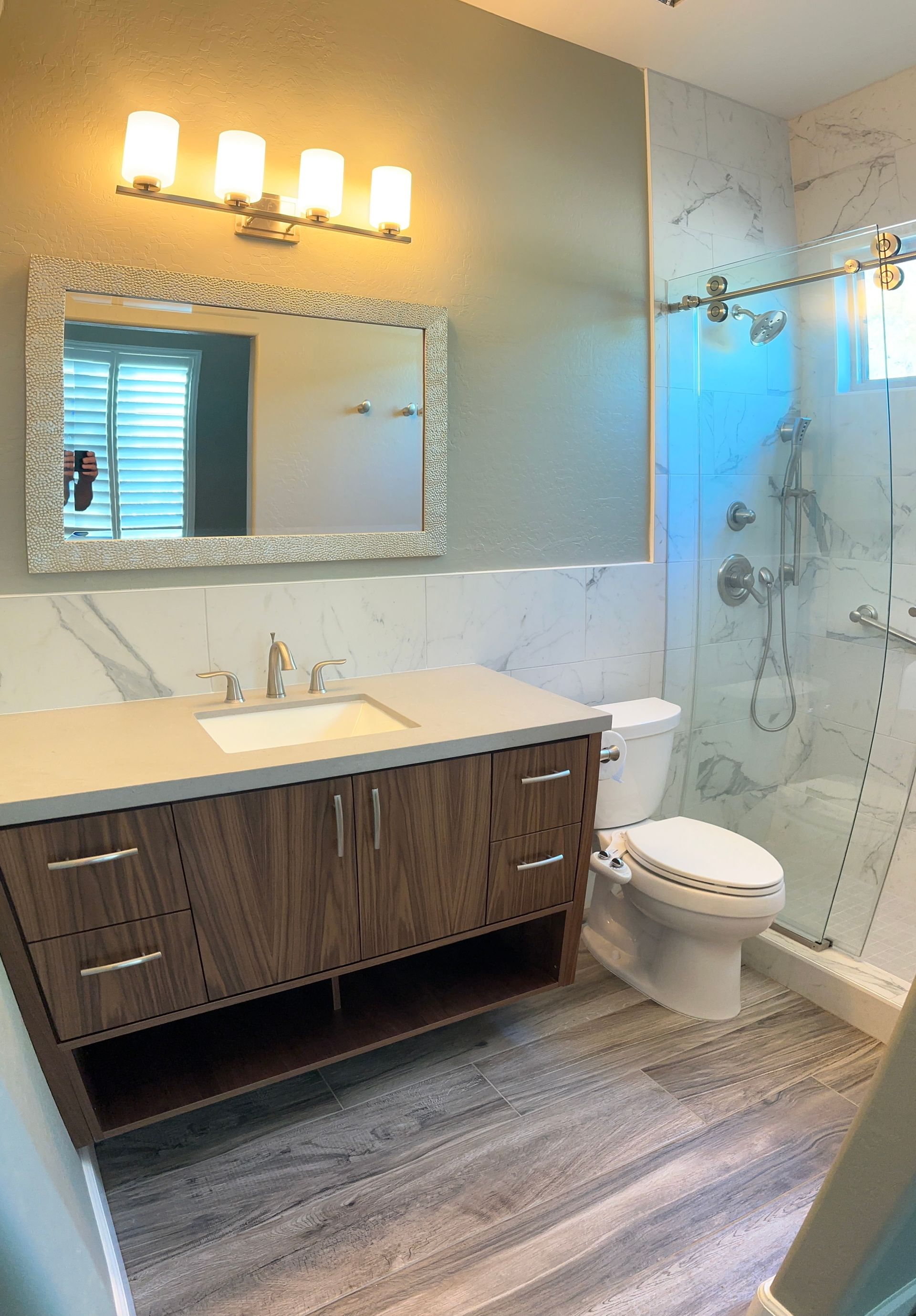A bathroom with a toilet , sink , mirror and shower.