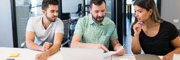 A group of people are sitting at a table looking at a laptop computer.