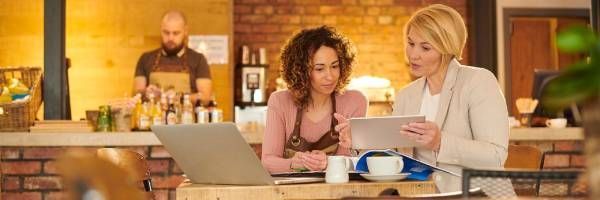 Two women are sitting at a table with a laptop and a tablet.