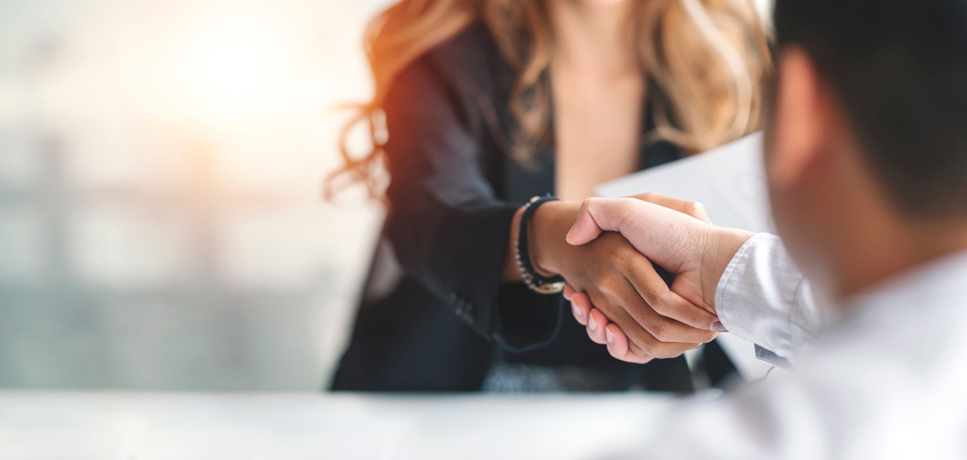 A man and a woman are shaking hands at a table.