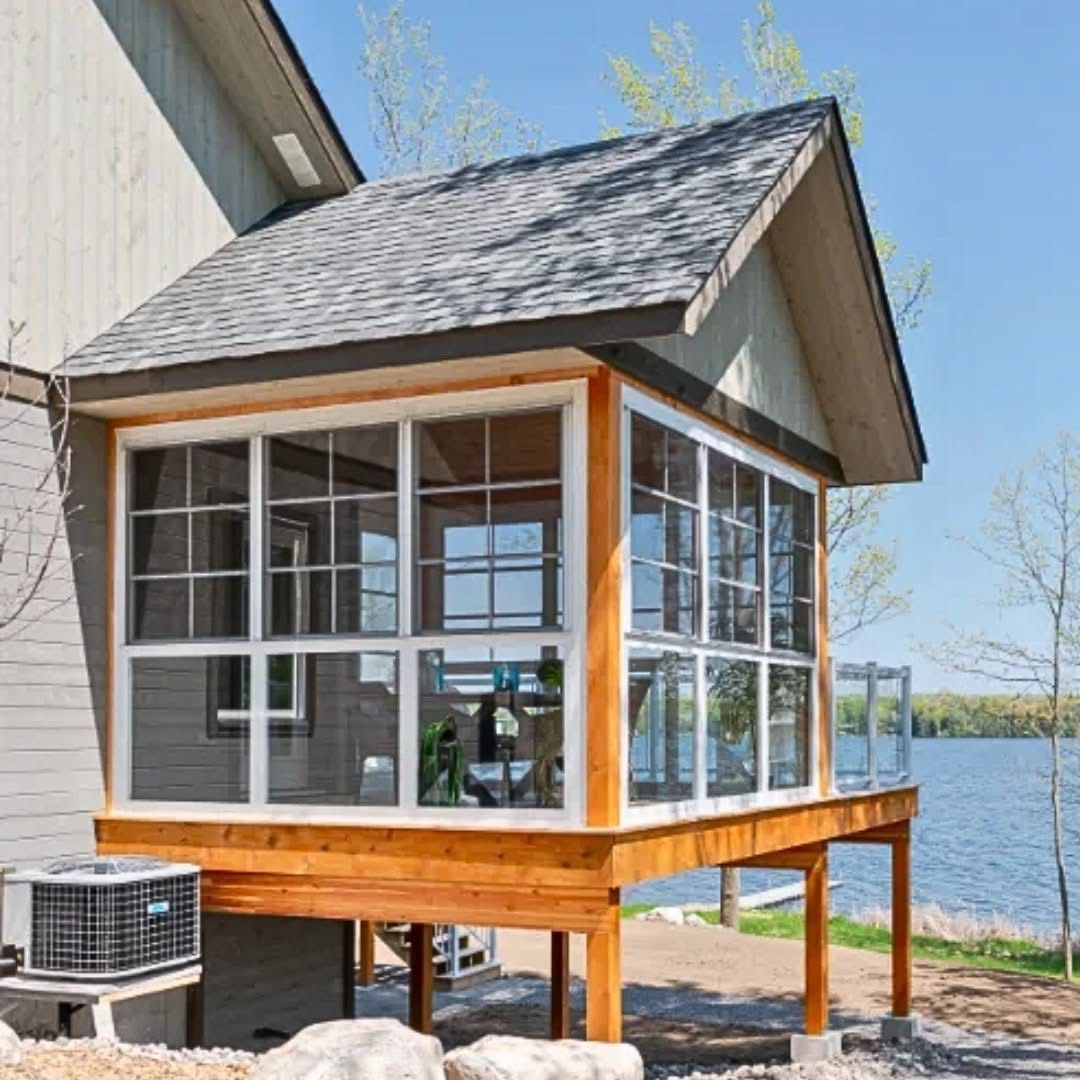 Screened porch with windows, wooden deck, gray roof, on a lake, visible air conditioner.